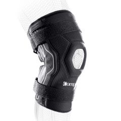 Ceļa ortoze Compex Bionic – melna elpojoša ceļgala saite ar sešstūra patellas atvērumu, silikona joslām un atstarojošu lenti; attēls uz balta fona.